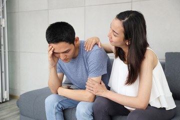 young pregnant wife comforting and touching shoulder young husband while sitting on sofa