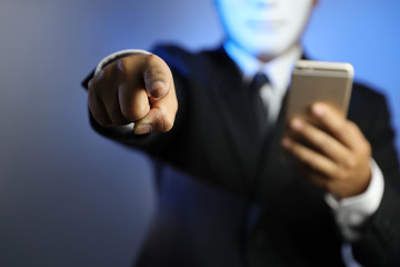 employee or businessman wearing black suit and mask with cell phone hacking and stealing big data and pointing at something meaning for warning