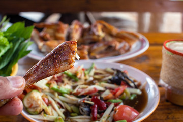 Hand holding the grilled chicken with papaya salad or somtum and sticky rice in wicker basket