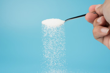 Naklejka na ściany i meble Hand pouring sugar from spoon isolated on blue background
