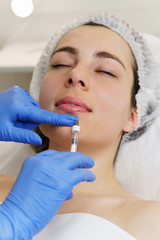 Aesthetic cosmetology. Hands cosmetologist injections of hyaluronic acid in lower lip girl. Lip augmentation.