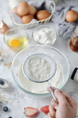 Making pancakes, cake, baking of baker hands sifting flour in bowl. Concept of Cooking ingredients and method on white marble table. Dessert recipes and homemade.