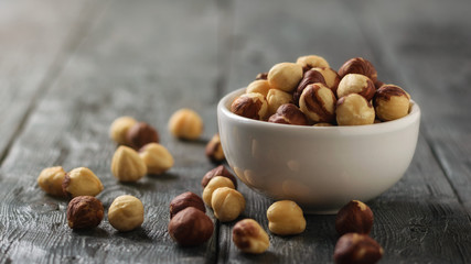 Ceramic bowl with roasted hazelnuts on the black table.