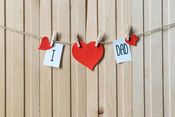 Fathers day concept. Message with paper hearts hanging with pins over light wooden board.