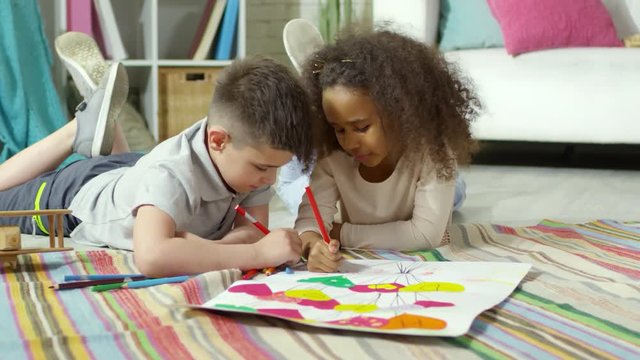 Little african girl and caucasian boy lying together on floor in kids room, talking and drawing greeting poster for Mothers Day