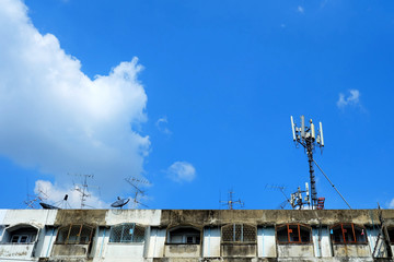 Telecom Poles and Satellites on Roofs with White Clouds and Blue Sky.