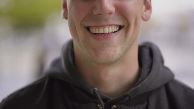 Cropped shot of cheerful young man laughing. Close-up partial view of handsome happy young man smiling outdoor, handheld shot. Emotion concept