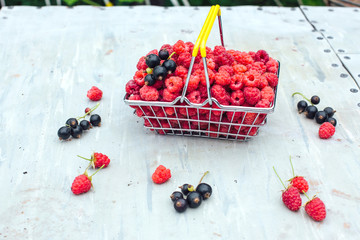 Mini shopping basket full of fresh red ripe raspberry and blackberry on vintage background