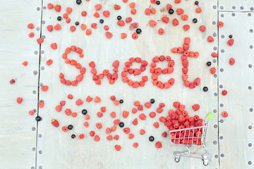 Word SWEET made of raspberry and mini shopping basket full of fresh red ripe raspberry on vintage...