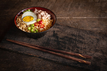 Instant noodle with pork, egg and vegetables on black bowl on the wood table there is chopstick placed in front of.