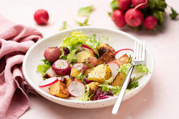 Healthy potato salad with radishes and green leaf lettuce on pink background