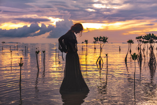 Young Woman Standing In Water At Sunset Silhouette