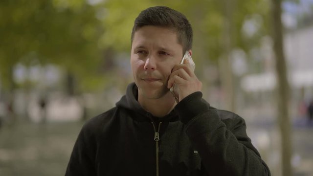 Happy young man talking by smartphone outdoor. Cheerful handsome young man walking on street and shaking fist uring pleasant phone conversation. Communication concept