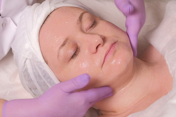 Obraz na płótnie Canvas Cosmetic procedure. Facial massage with a transparent gel. Woman with eyes closed. Beautician hands in pink gloves. Concept of skin rejuvenation, health and beauty.