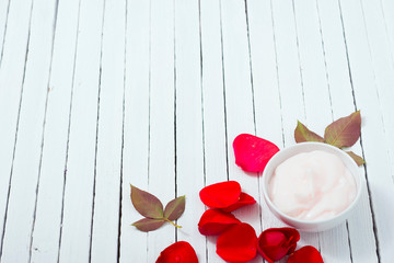 moisturizer and rose petals on white wood