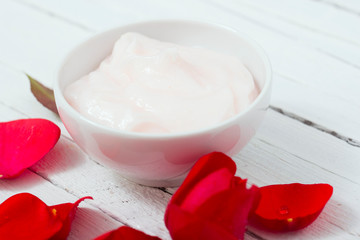 moisturizer and rose petals on white wood