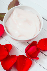 moisturizer and rose petals on white wood