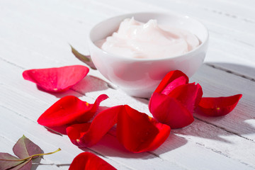 moisturizer and rose petals with shade on white wood