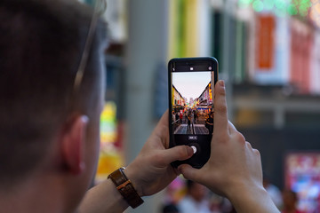 Male hands using smartphone taking a photo on the street at dusk.