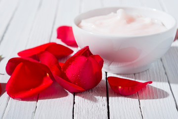 moisturizer and rose petals with shade on white wood