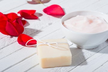 moisturizer, soap and rose petals on white wooden table