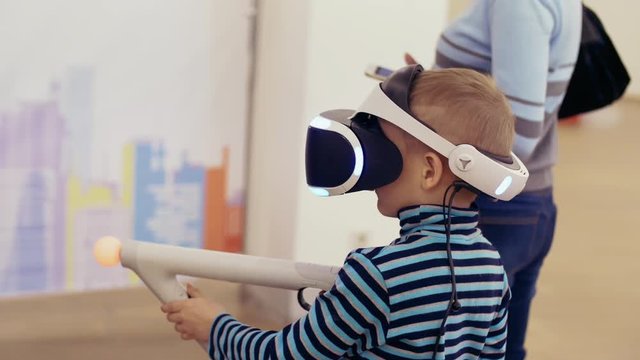 Children in an interactive VR helmet play video game. Boy in VR glasses of virtual reality playing game. 