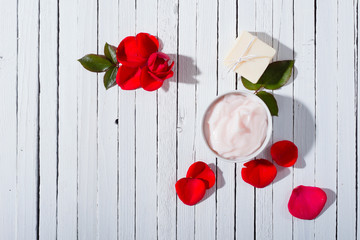 moisturizer, soap and rose petals on white wooden table