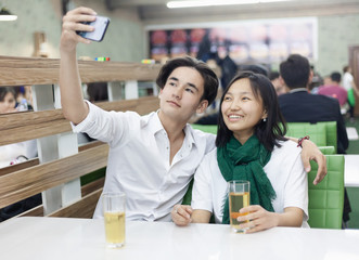 Asian teen friends couple are sitting in a cafe and having fun, taking a selfie on a mobile phone, watching social networks in the school cafeteria