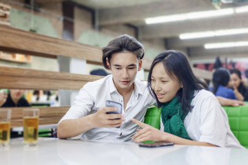 Asian teen friends couple sit in a cafe and have fun, watch social networks in the school cafeteria