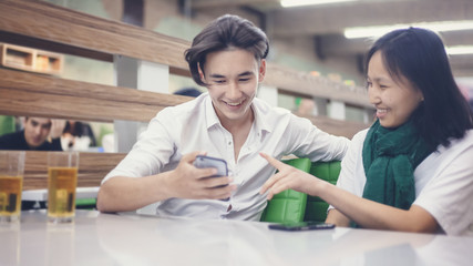 Asian teen friends couple sit in a cafe and have fun, boy and girl 15 years watching  social networks in the school cafeteria