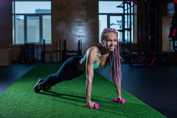 Beautiful athletic girl in colored sportswear posing in the gym. Young beautiful fitness model with African braids in the gym engaged in Pilates
