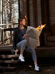 Young woman in a leather jacket checkered pants and white sneakers with a burning newspaper in her hands.