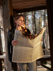 Young woman in a leather jacket checkered pants and white sneakers with a burning newspaper in her hands.