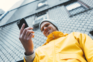 Young man in yellow raincoat using mobile phone while standing on the city street © Alex from the Rock