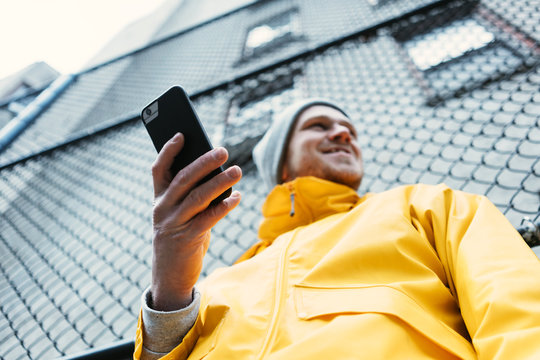Smiling man in yellow raincoat using mobile phone while standing on the city street