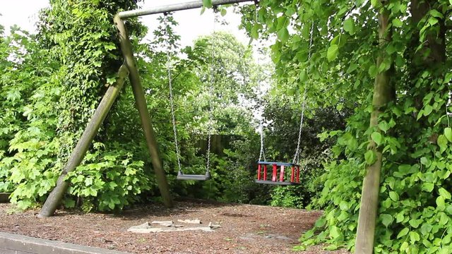 Angle number two a childrens playground swing is swinging by itself with no child in sight this angle shows the whole swing set set in a green folayage