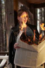 Young woman in a leather jacket checkered pants and white sneakers with a burning newspaper in her hands.