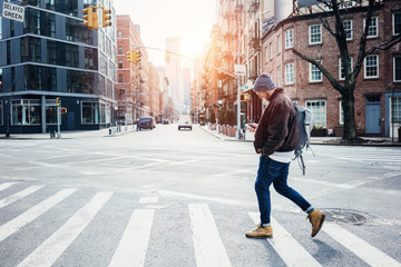 Man wearing hat and jacket walking on the city crossroad with mobile phone in hand