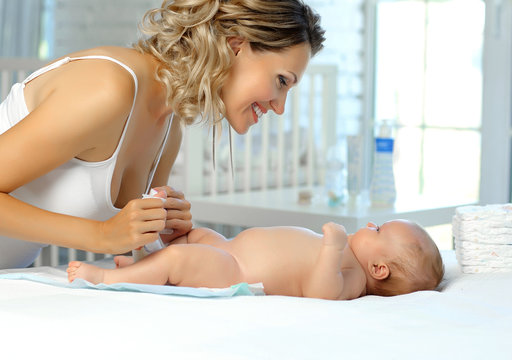 The Mother Changes The Diaper To The Newborn And Smiles At Him