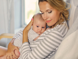 Portrait of mother and her 2-month-old child. Blonde hair, striped clothes.