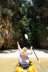 Blonde Caucasian woman paddling in kayak towards secluded tocky beach at Krabi, Thailand