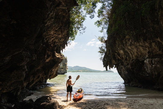 Man with a paddle standing next to sea kayak at secluded beach in Krabi, Thailand