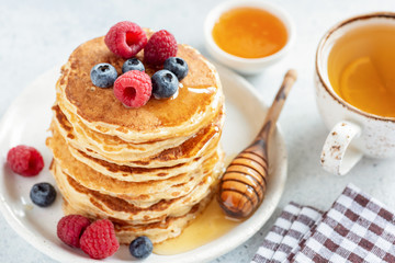 Homemade pancakes topped with berries and honey served with cup of green tea with lemon. Closeup view. Tasty breakfast food