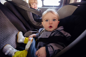 Cute girl and boy sitting in car back seat in a child safety seat