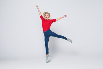 Fototapeta premium Full length portrait of woman wearing jeans and t-shirt jumping and rejoicing with perfect smile isolated over gray background