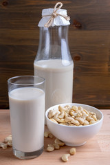 Glass of Cashew milk and bottle and organic cashew on wooden background, Alternative Milk