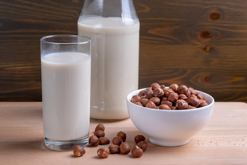 Glass of Hazelnut milk and bottle and organic hazelnuts on wooden background, Alternative Milk. Nuts milk