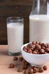 Glass of Hazelnut milk and bottle and organic hazelnuts on wooden background, Alternative Milk. Nuts milk