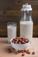 Glass of Hazelnut milk and bottle and organic hazelnuts on wooden background, Alternative Milk. Nuts milk
