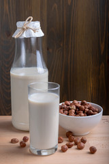 Glass of Hazelnut milk and bottle and organic hazelnuts on wooden background, Alternative Milk. Nuts milk